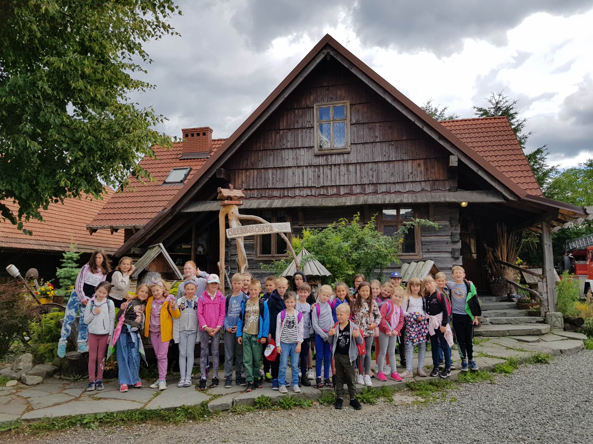 Grupa dzieci stojących przed drewnianym domem