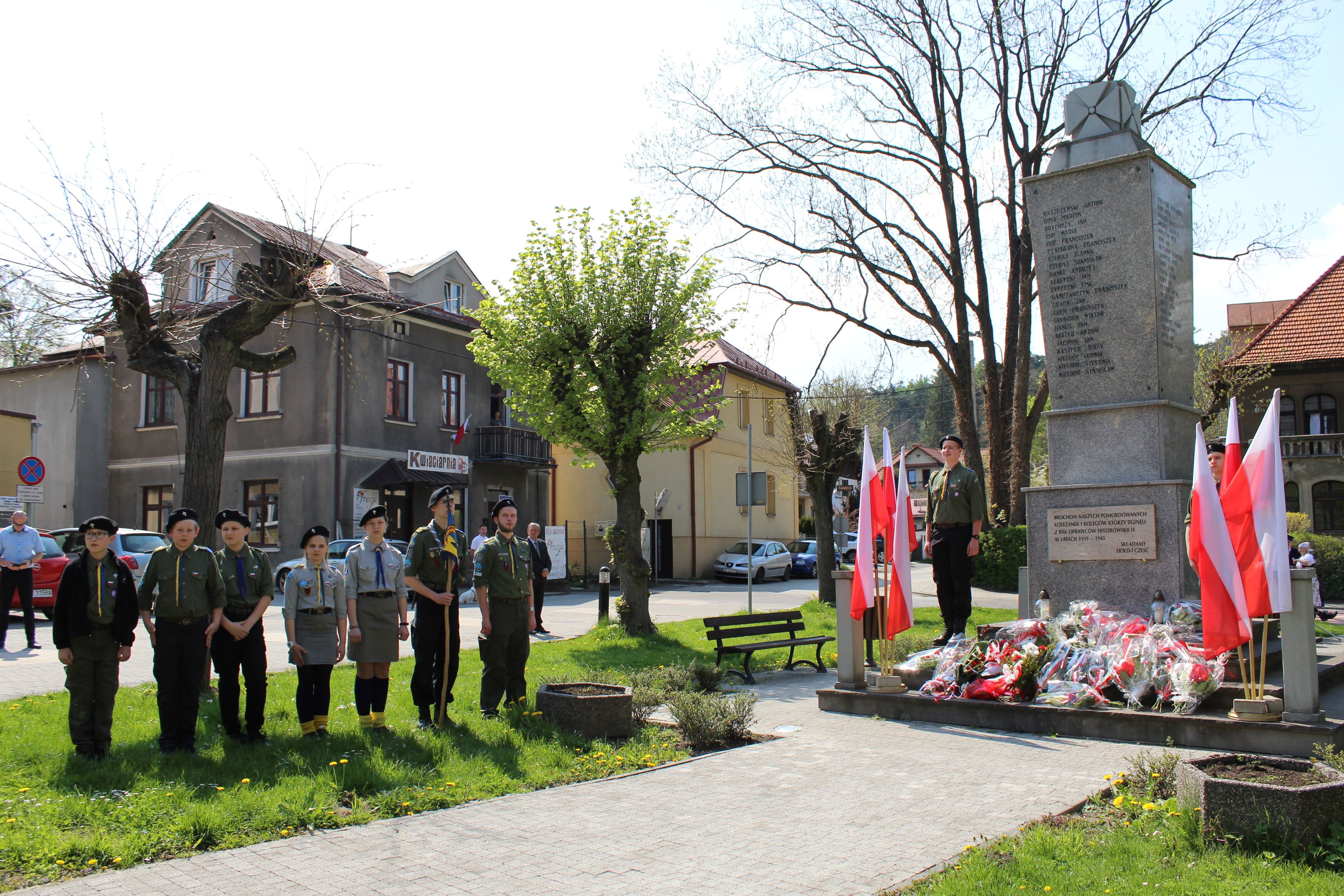 Harcerze stojący przed pomnikiem. Obok flagi Polski. Pod pomnikiem kwiaty.