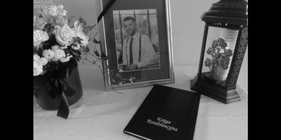 Księga kondolencyjna leżąca na stoliku, obok kwiaty oraz zdjęcie wójta przepasane kirem