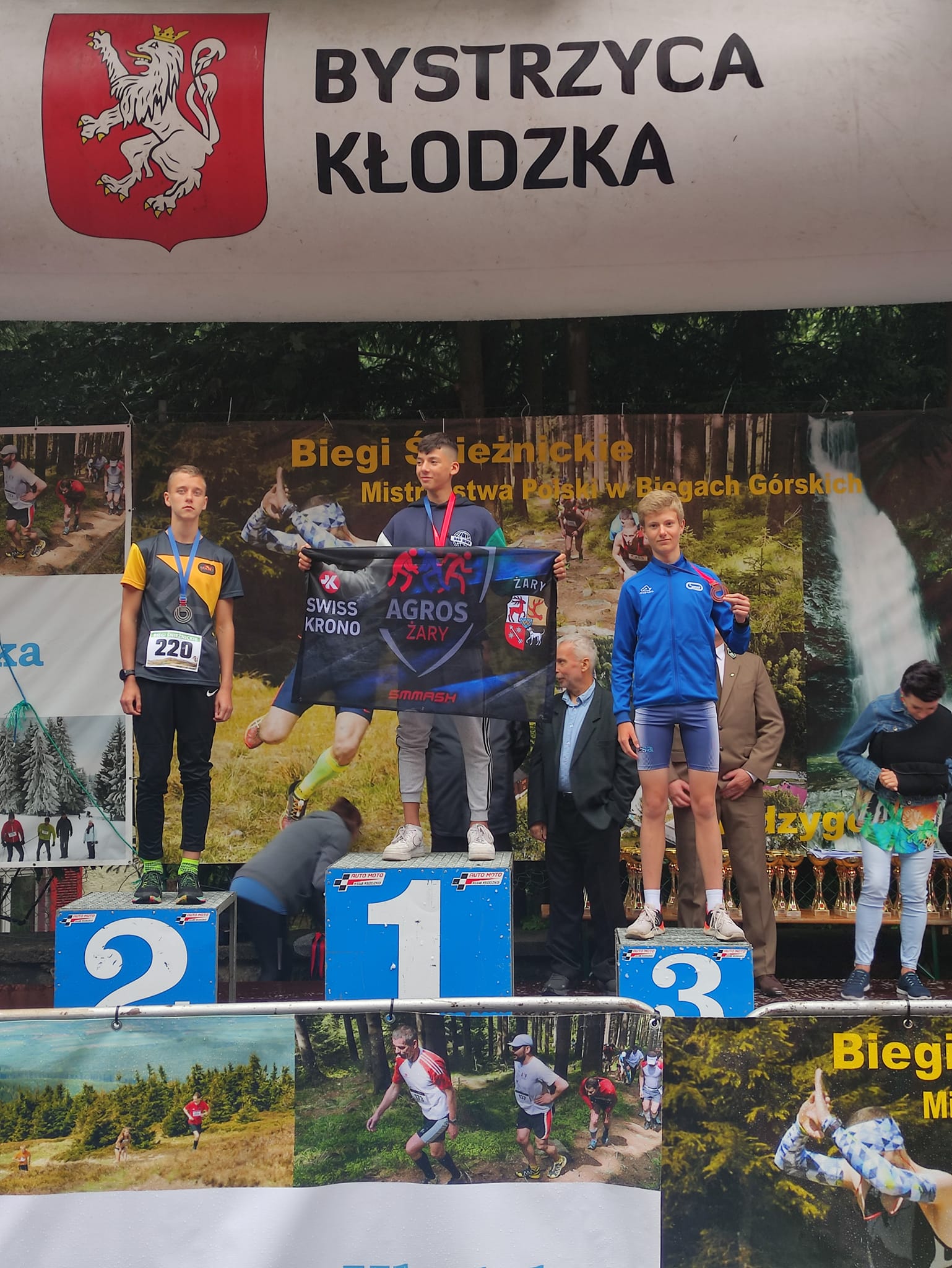 Podium sportowe, na którym stoi trzech chłopców w strojach sportowych. W ręku trzymają medale