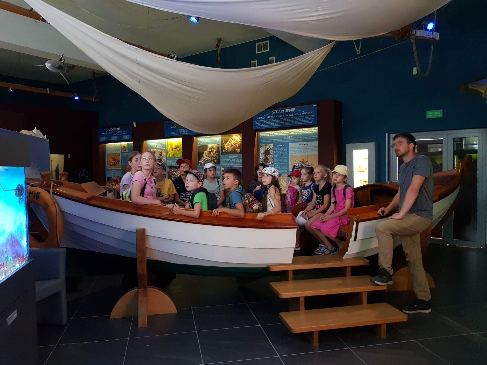 Grupa dzieci siedząca w drewnianej łodzi w muzeum