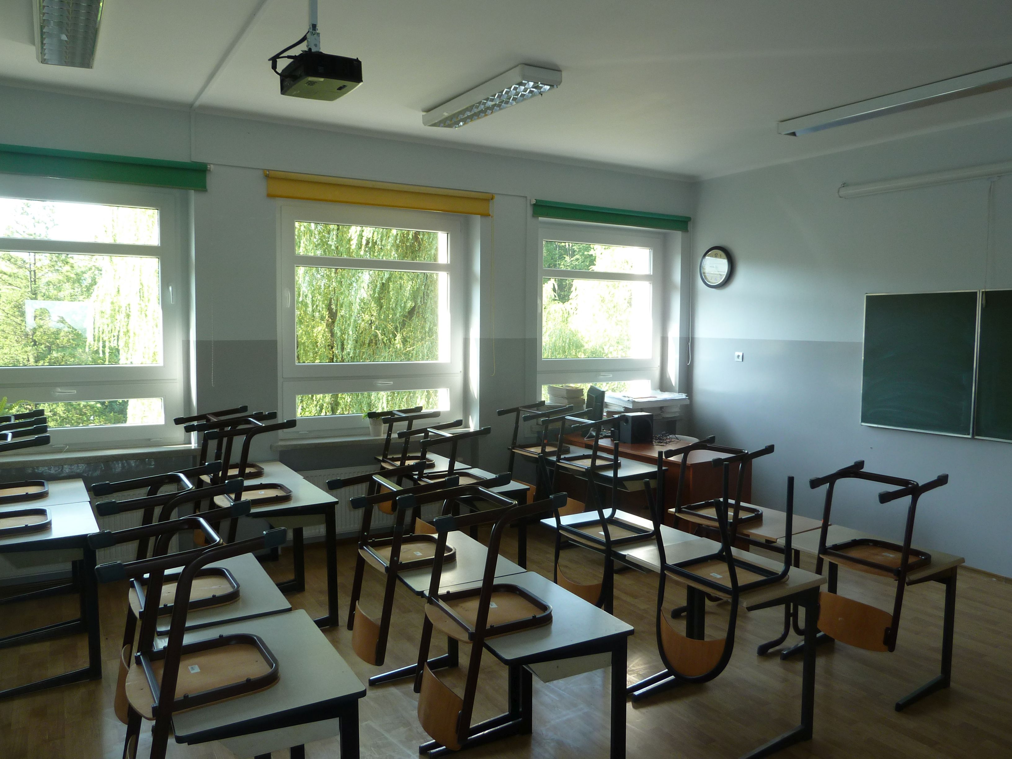 Sala szkolna, krzesła ustawione na ławkach, widok w stronę okien