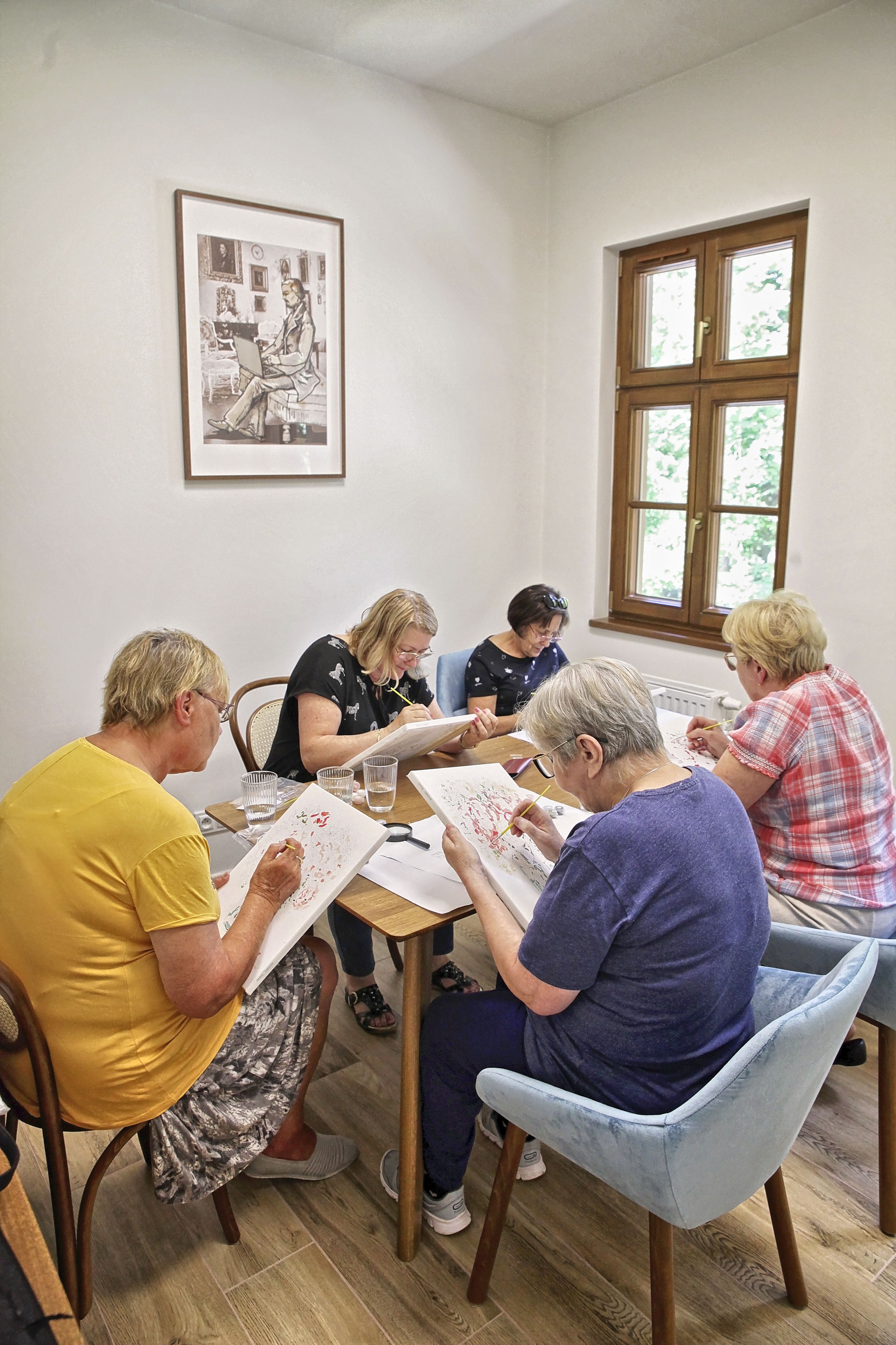 uczestnicy warsztatów wykonujący prace plastyczne, siedzący przy wspólnym stoliku