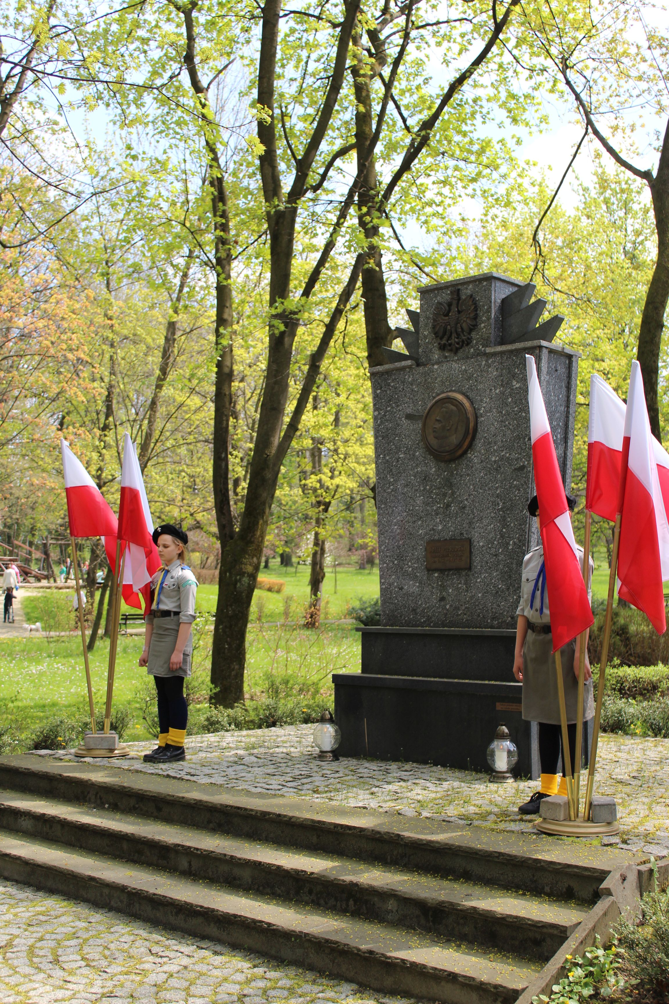 Harcerze stojący przed pomnikiem. Obok nich flagi Polski.