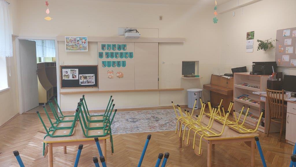 Sala przedszkolna, drewniany parkiet, na środku ławki, na parkiecie dywan