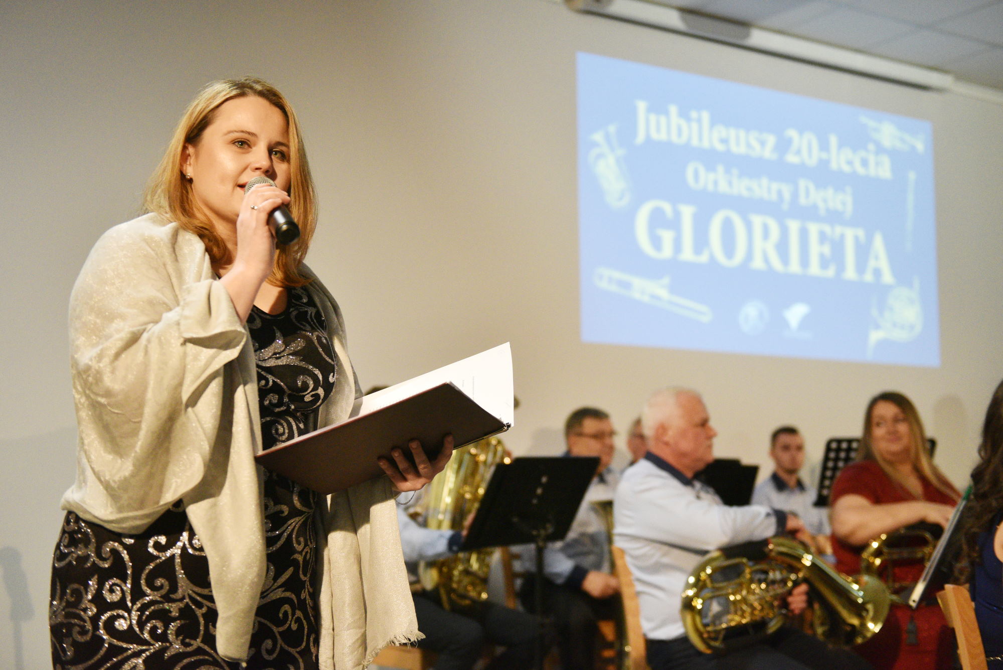 Kobieta śpiewająca do mikrofonu, z tyłu napis Orkiestra Dęta Glorieta