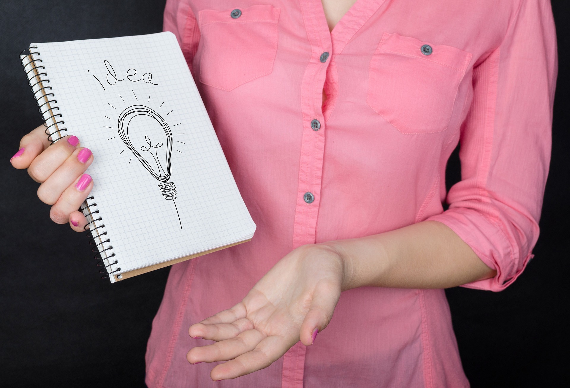 Kobieta trzymająca zeszyt, w którym narysowana jest żarówka i napis idea